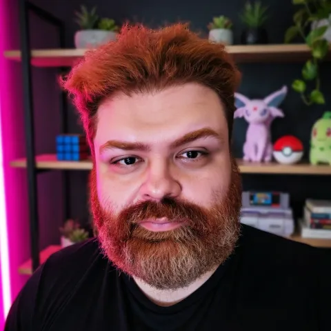 Hans Spiller, de cabelo e barba ruivos e camiseta preta, em frente a uma estante.